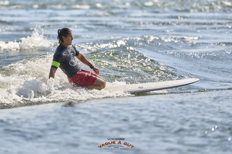 Un surfeur en short rouge, accroupi sur son longboard