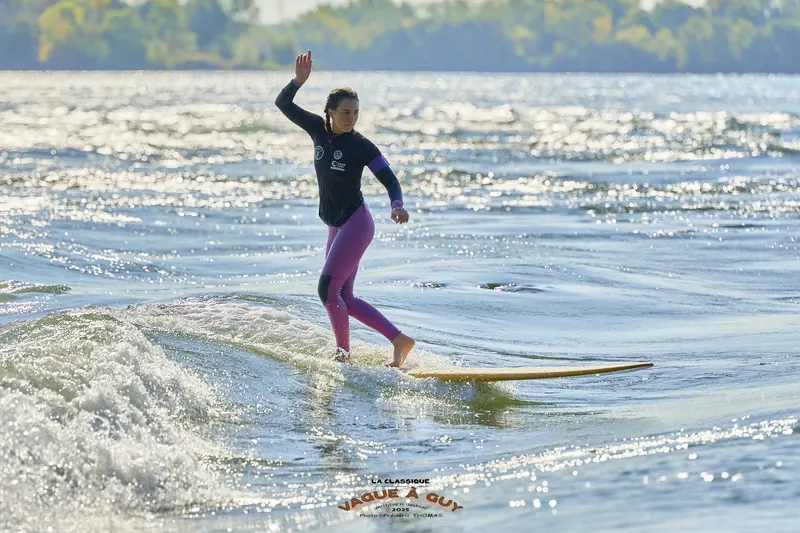 Une surfeuse en legging mauve, un bras levé, sur la vague