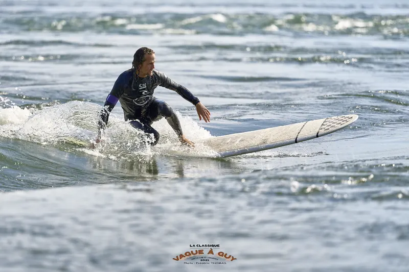 Un surfeur, bras en croix, en pleine manœuvre sur la vague