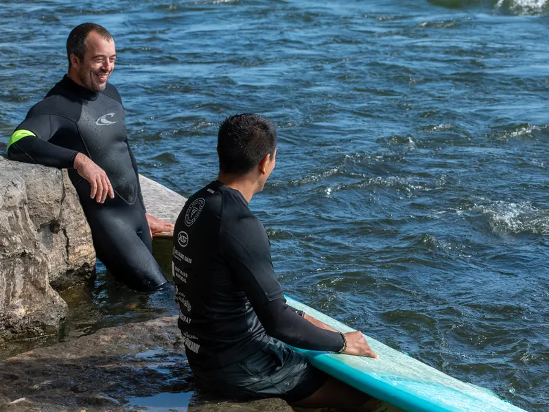 Deux surfeurs assis sur les rochers au bord du Saint-Laurent, planche turquoise à leurs pieds